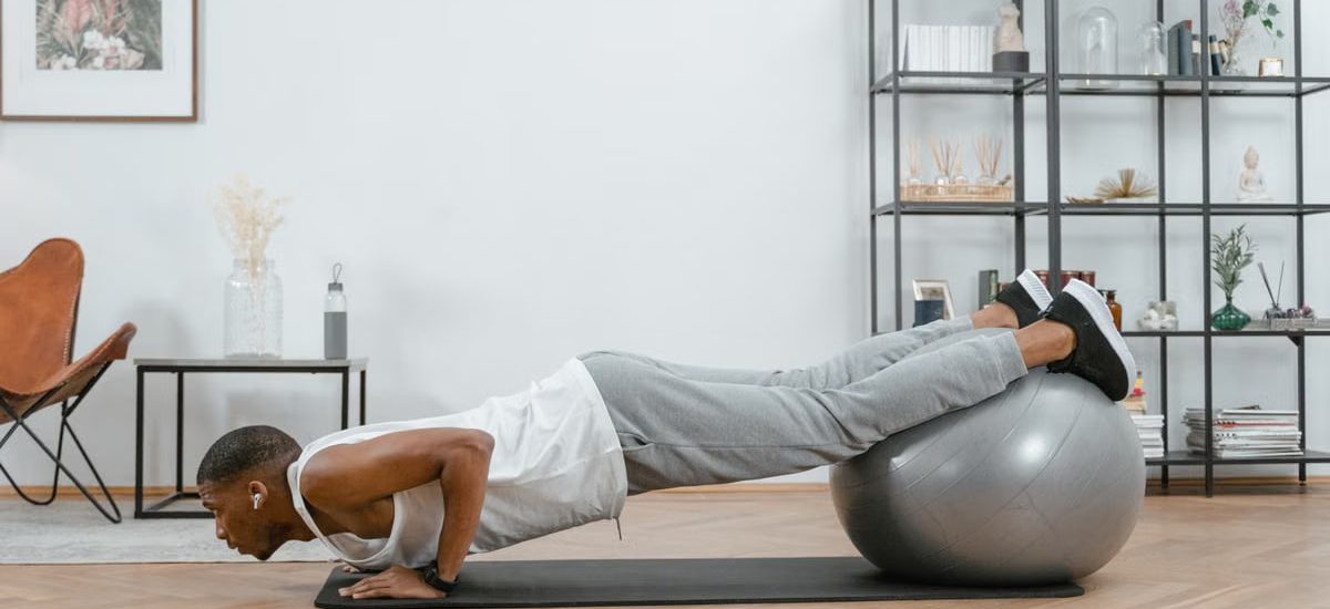 Adult doing push-ups with an exercise ball indoors for fitness and health.