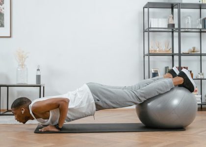 Adult doing push-ups with an exercise ball indoors for fitness and health.