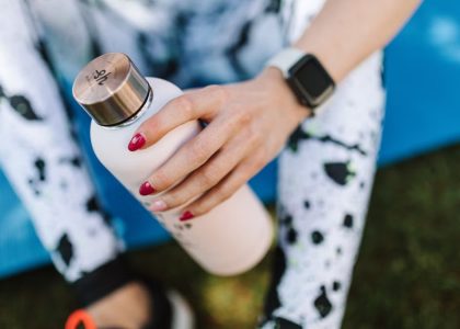 Crop unrecognizable female wearing sports leggings smart watch and holding bottle with water while relaxing after training on mat outside